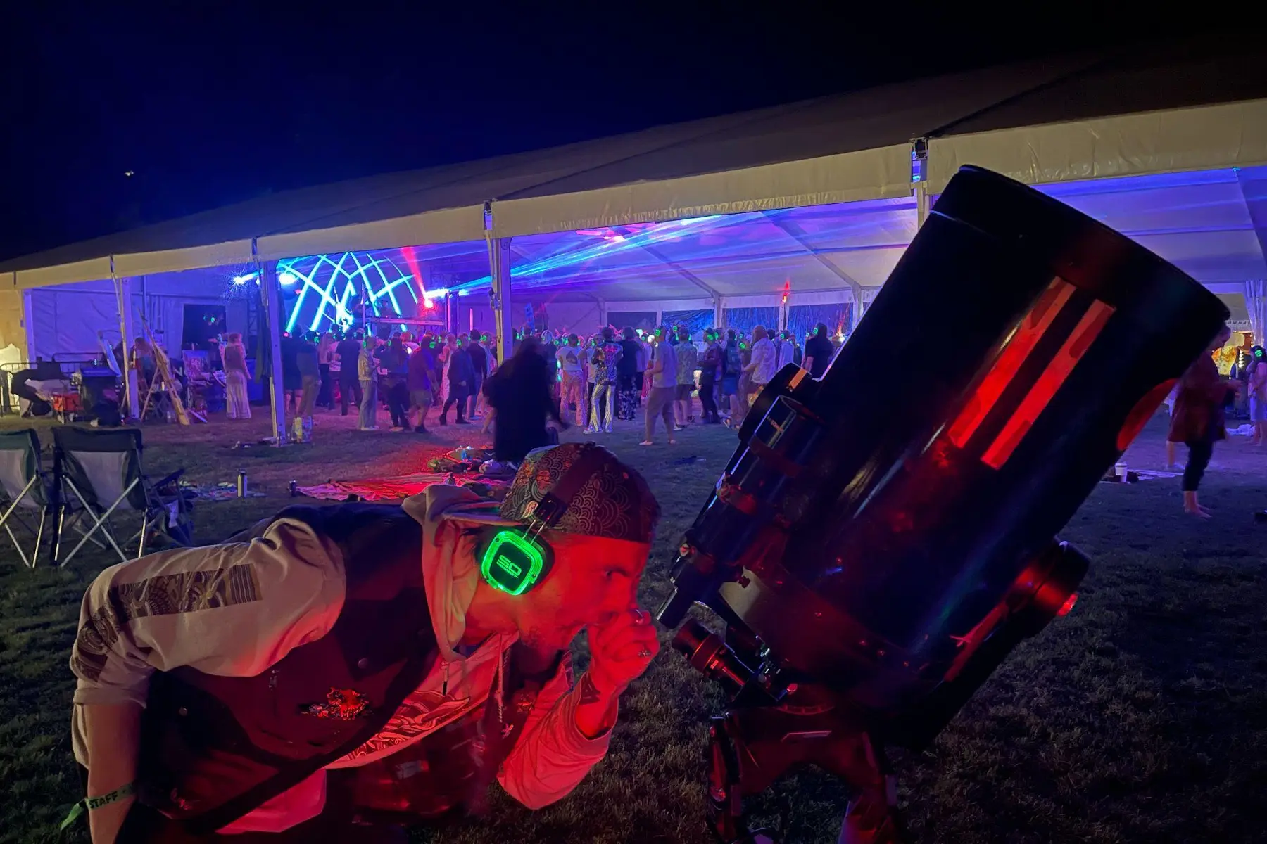 A guest looking through a large telescope during a busy nighttime festival program